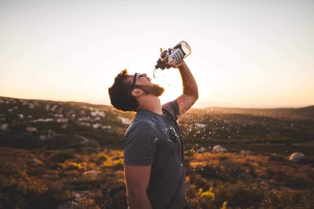 Un homme boit de l'eau en montagne