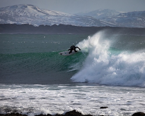 femme qui surf dans l'ocean avec montagnes enneigées