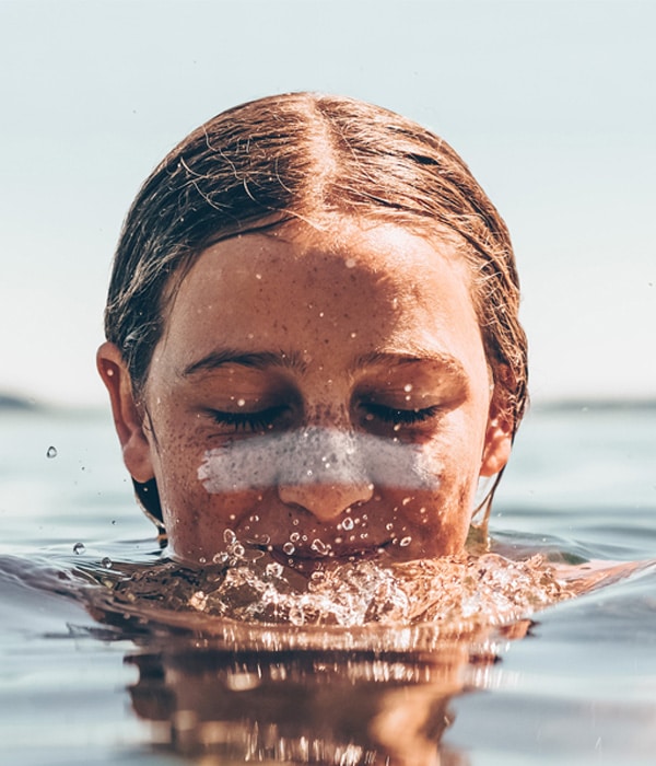 fille qui souffle dans l'eau avec stick solaire sur les joues