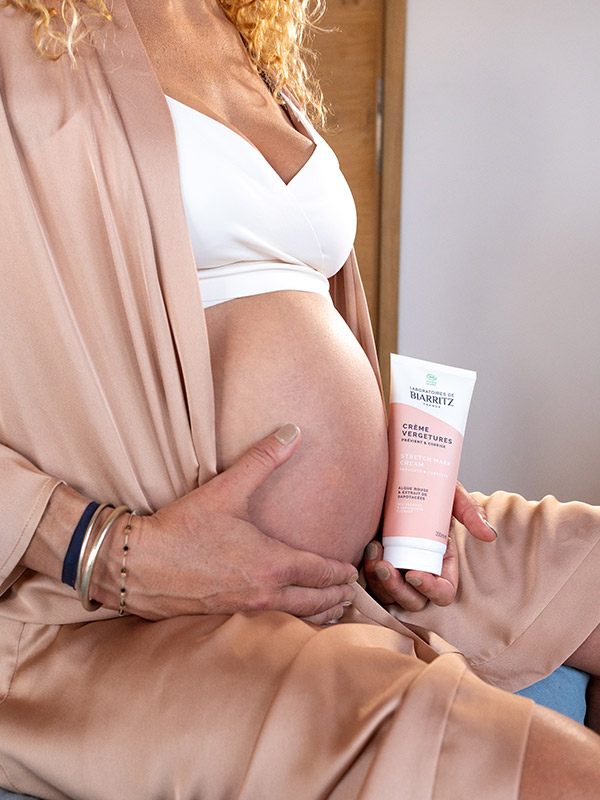 femme enceinte qui tient une crème vergetures dans les mains