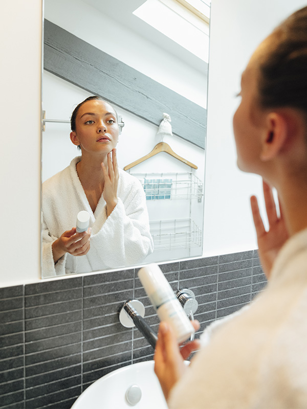 Femme qui s'applique de la crème devant le miroir dans la salle de bain